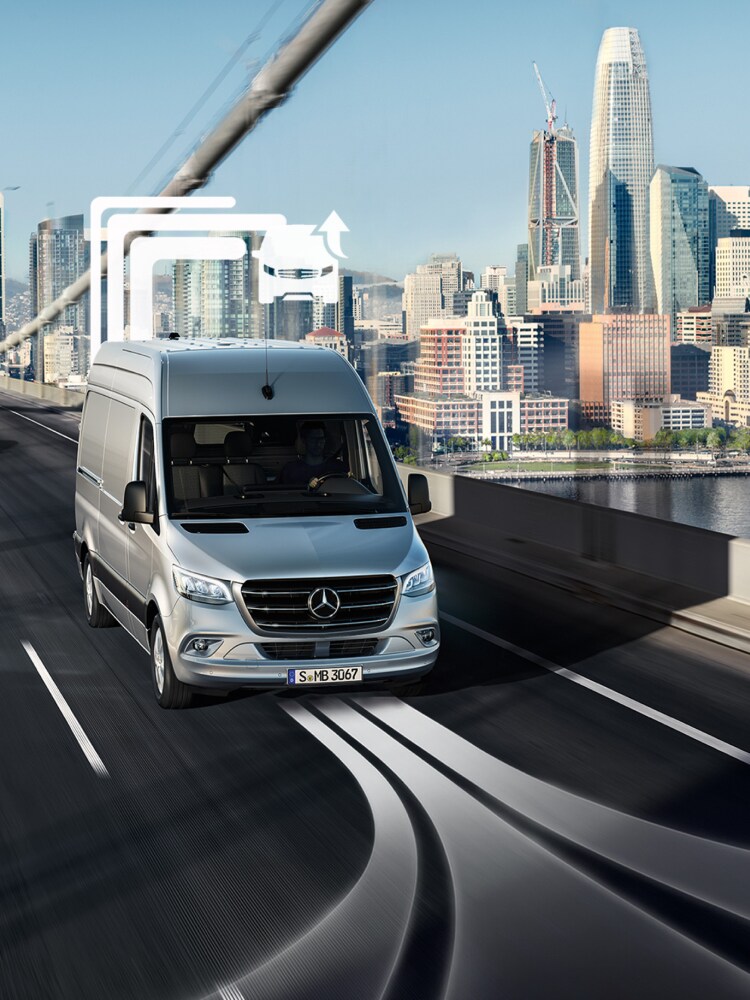 En Mercedes-Benz varevogn køres over en bro med skyline i baggrunden.