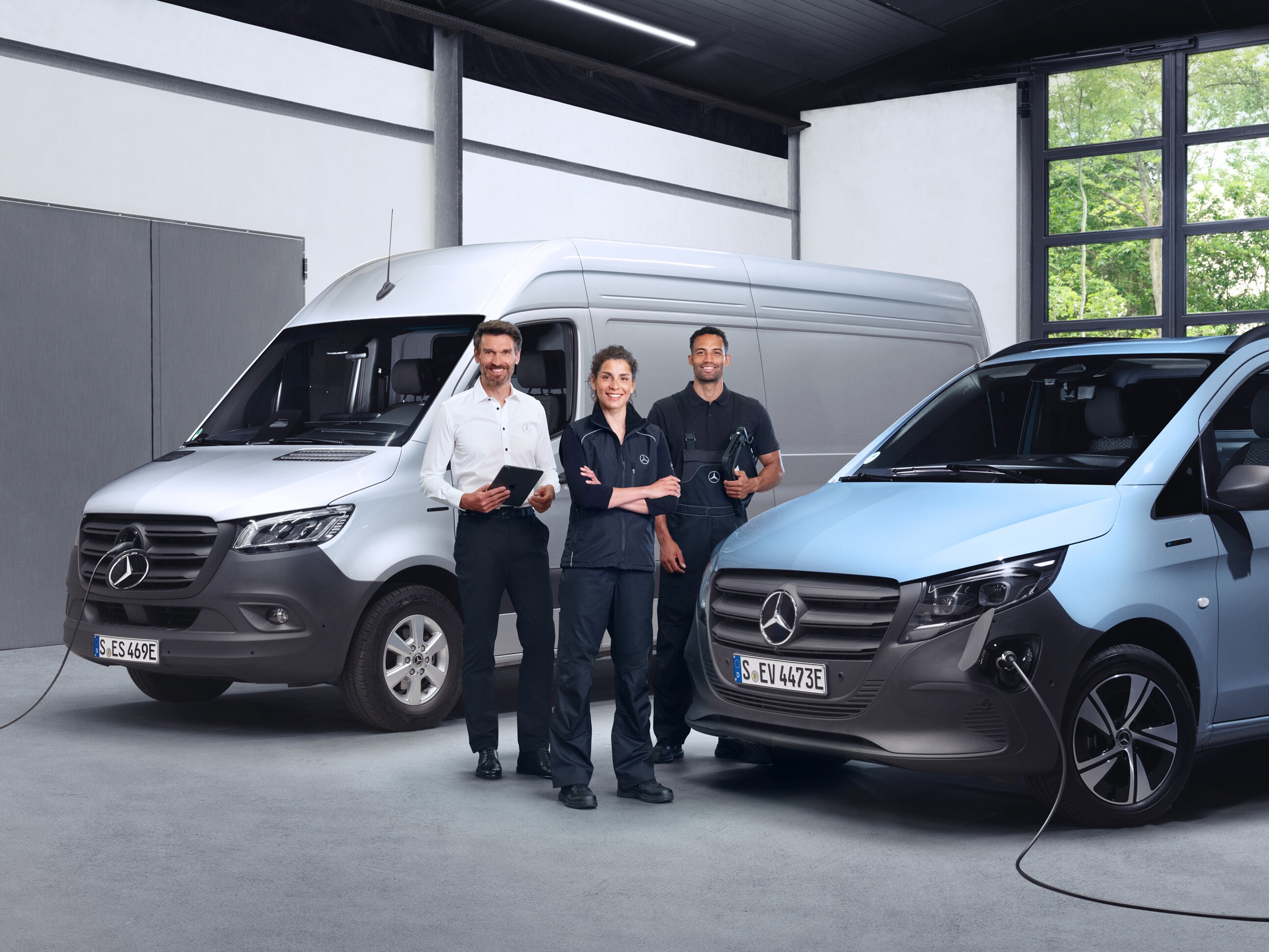 Tre medarbejdere foran to elektriske Mercedes-Benz varebiler.