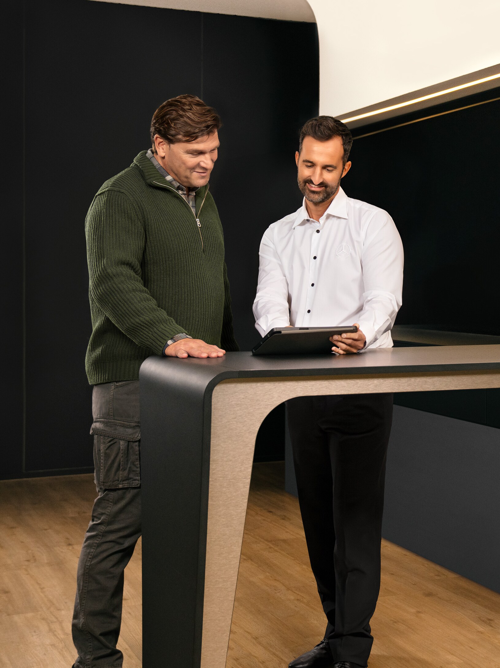 To mænd, der har en samtale, står omkring et bord og kigger på en tablet.