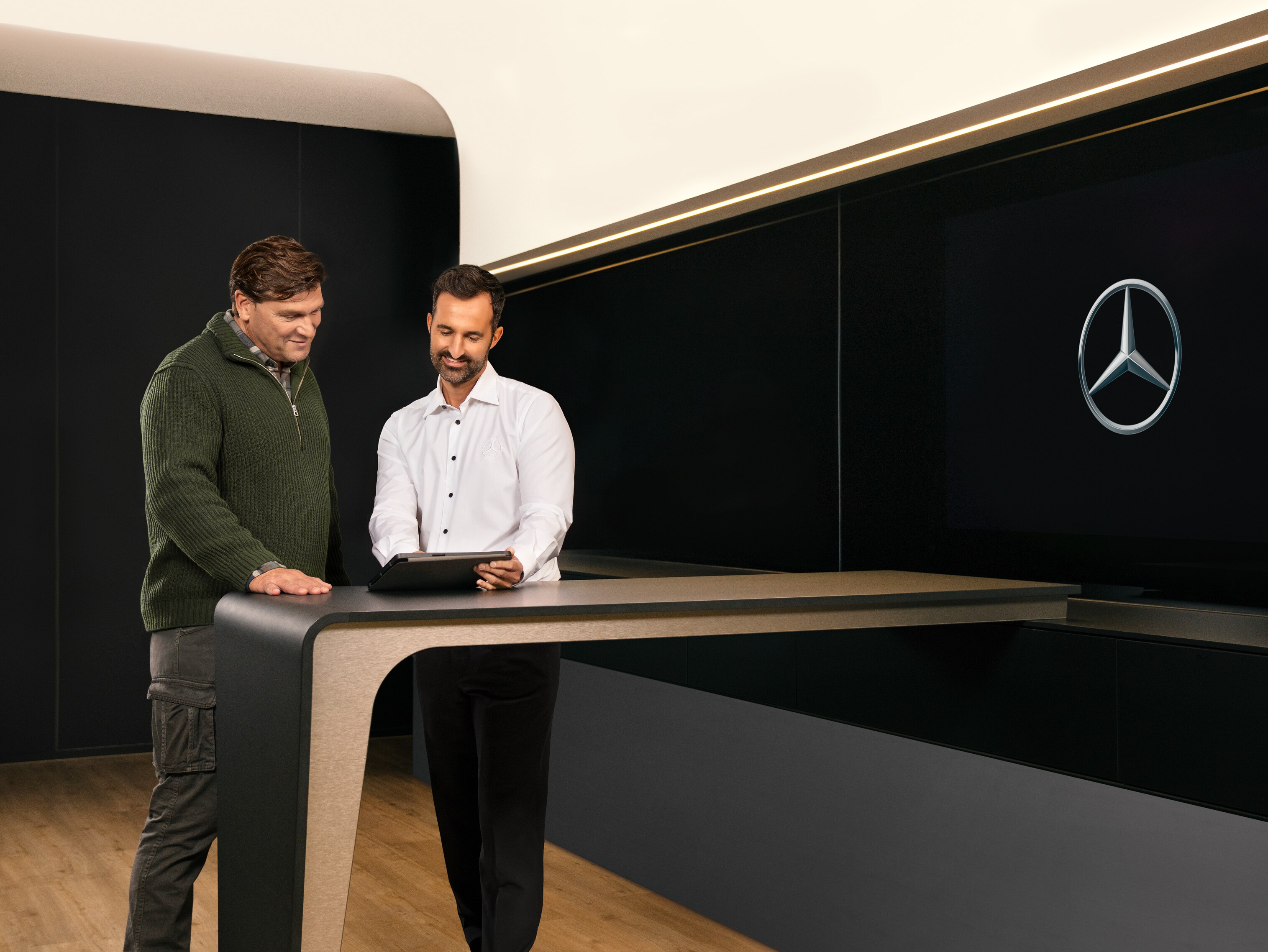 To mænd, der har en samtale, står omkring et bord og kigger på en tablet.