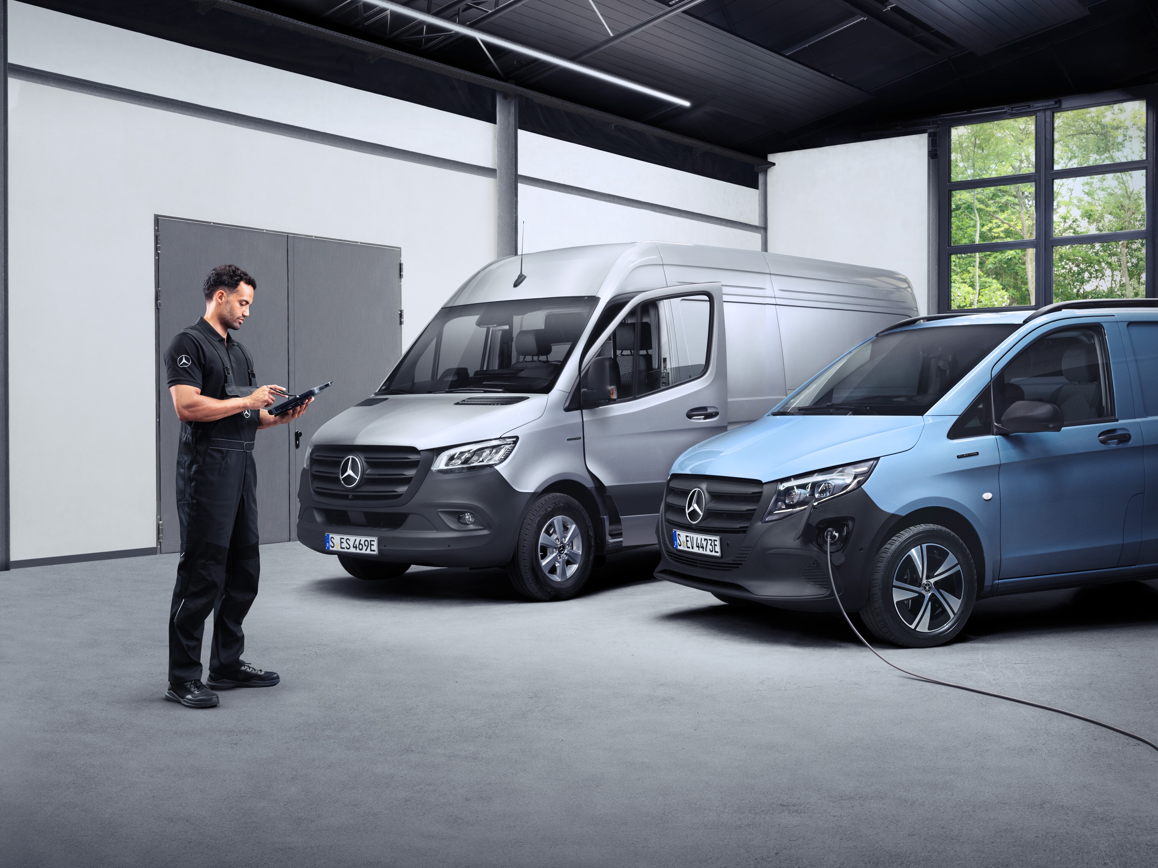 Mercedes-Benz tekniker med en tablet i hånden foran to elektriske varebiler.
