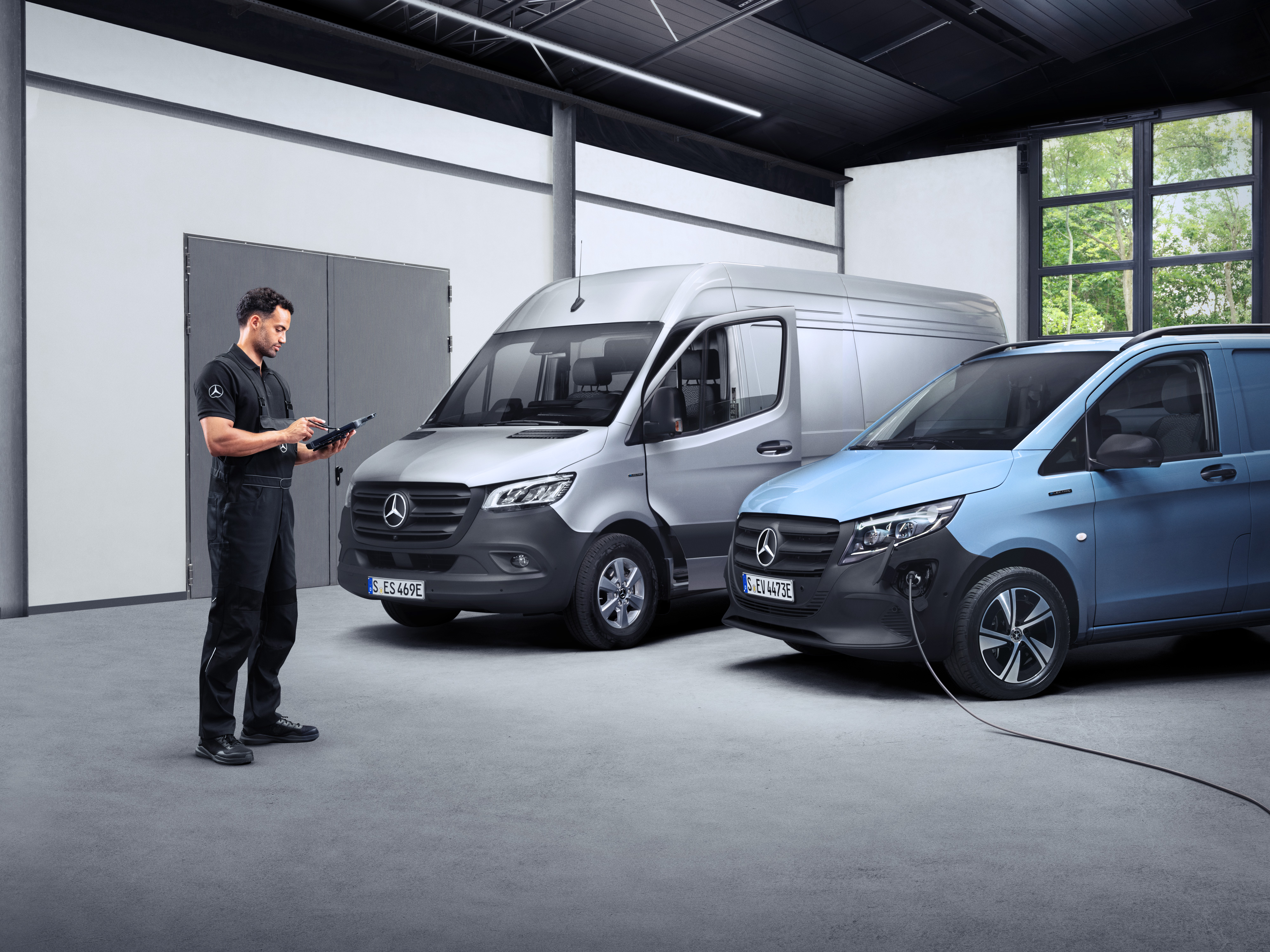 ServiceCare til varebiler | Mercedes-Benz varebiler Mercedes-Benz tekniker med en tablet i hånden foran to elektriske varebiler.