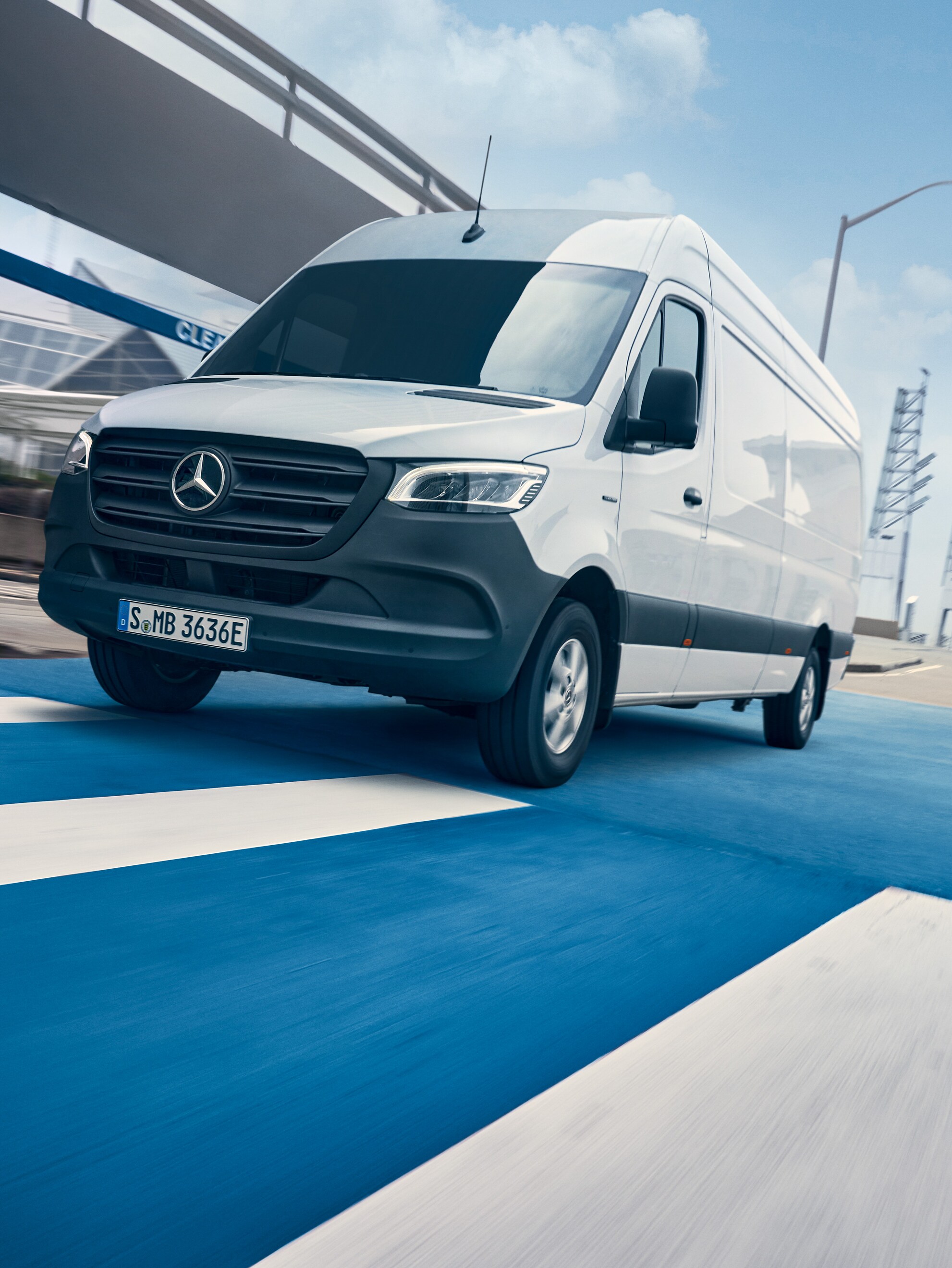 En hvid Mercedes-Benz Sprinter kører på en vej gennem en by.