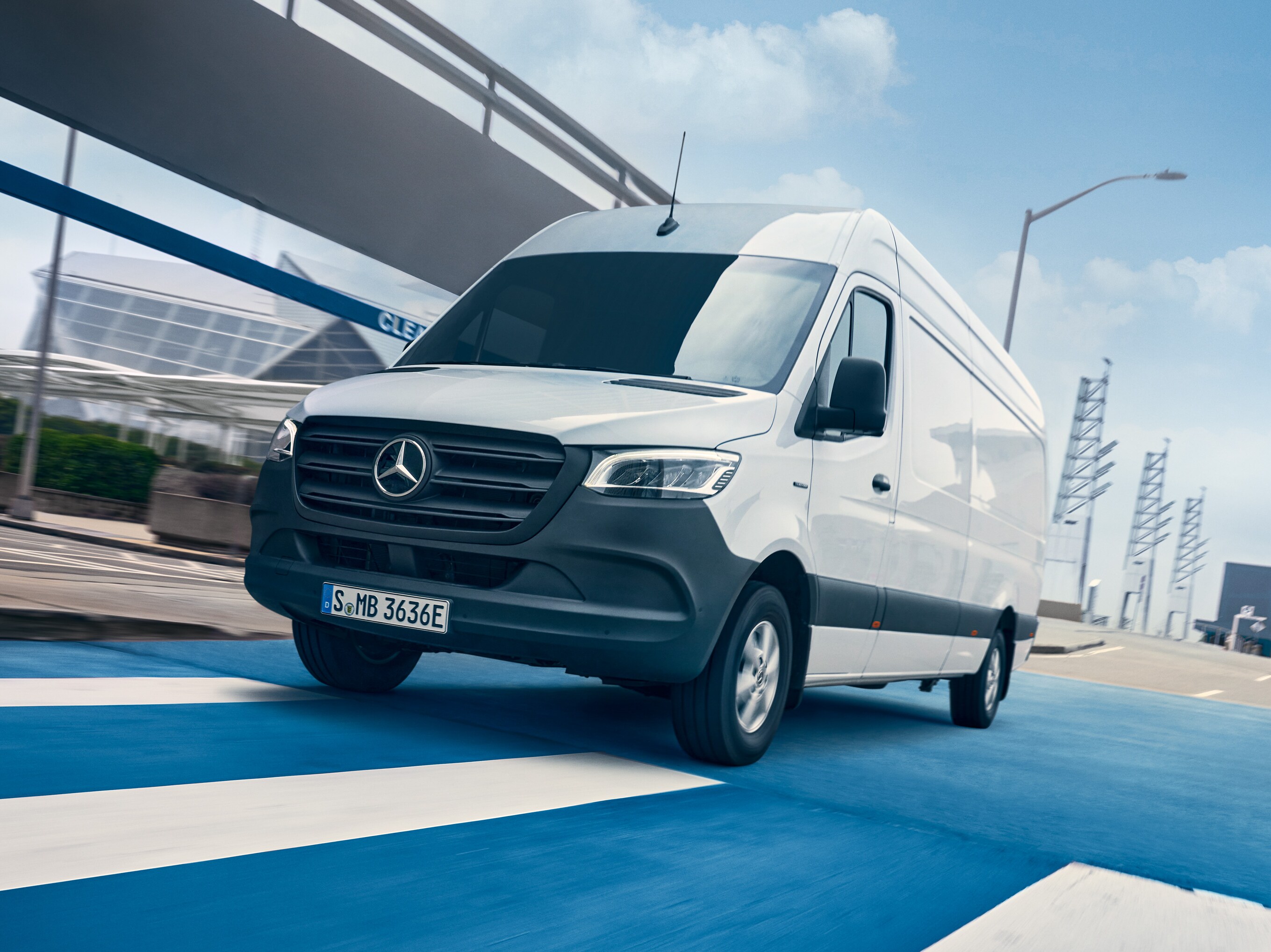 En hvid Mercedes-Benz Sprinter kører på en vej gennem en by.