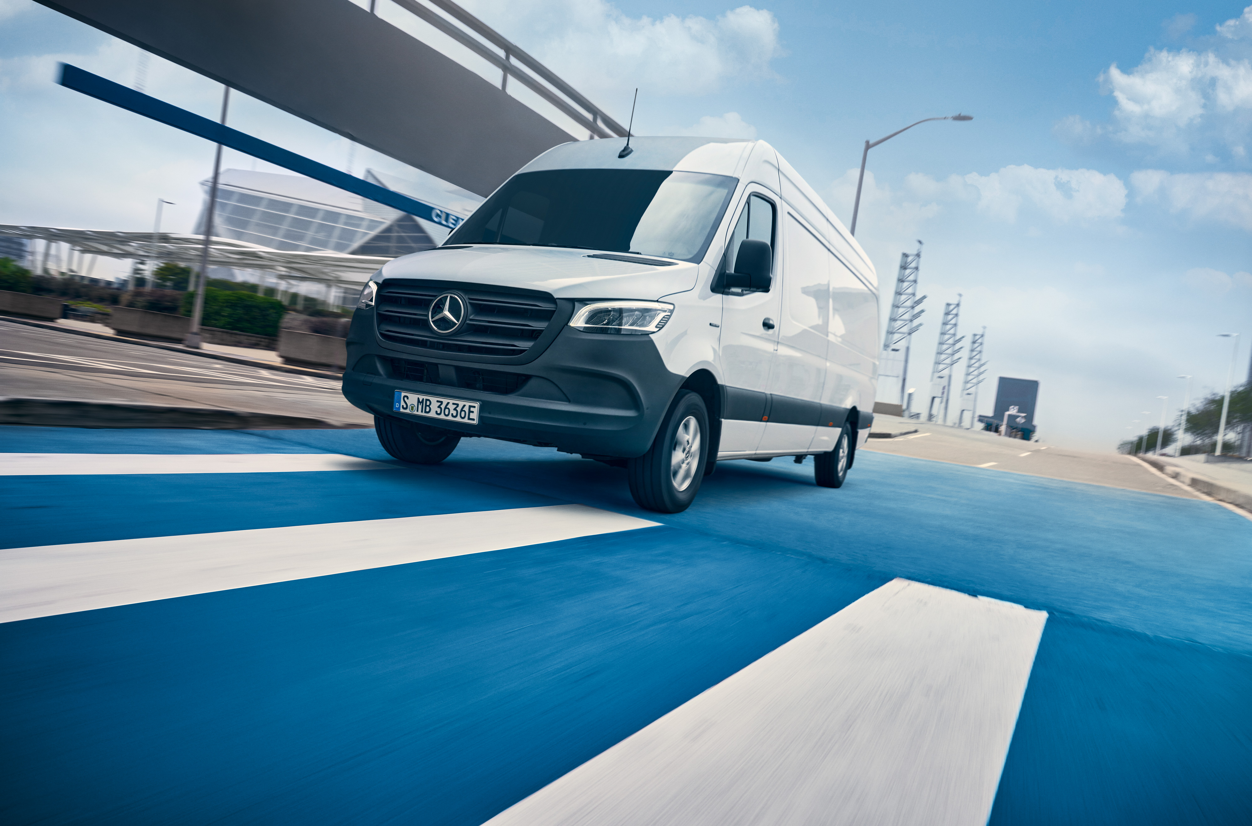 ServiceCare til varebiler | Mercedes-Benz varebiler En hvid Mercedes-Benz Sprinter kører på en vej gennem en by.