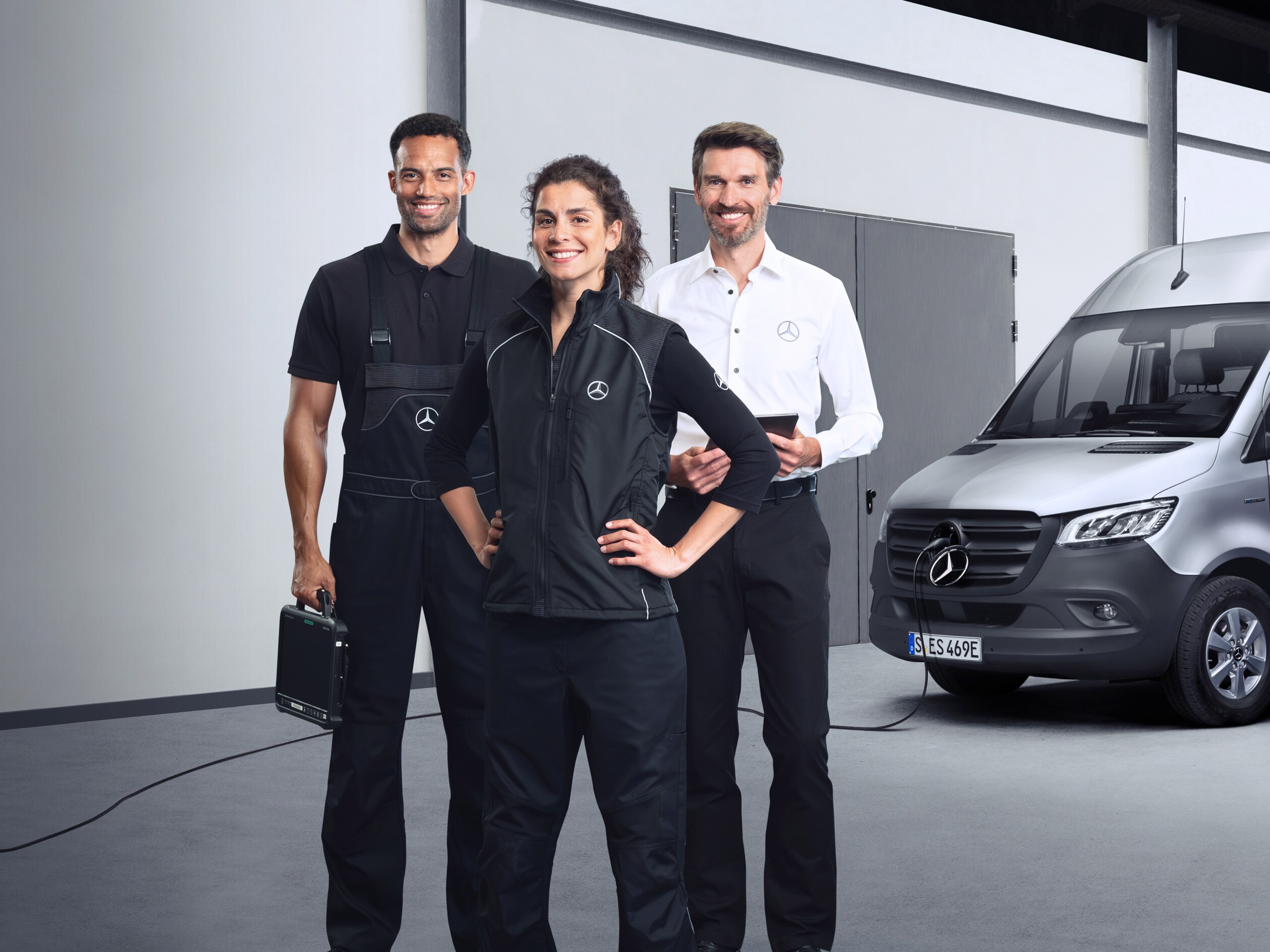 Tre medarbejdere står foran en sølvfarvet Mercedes-Benz eSprinter med isat ladekabel.