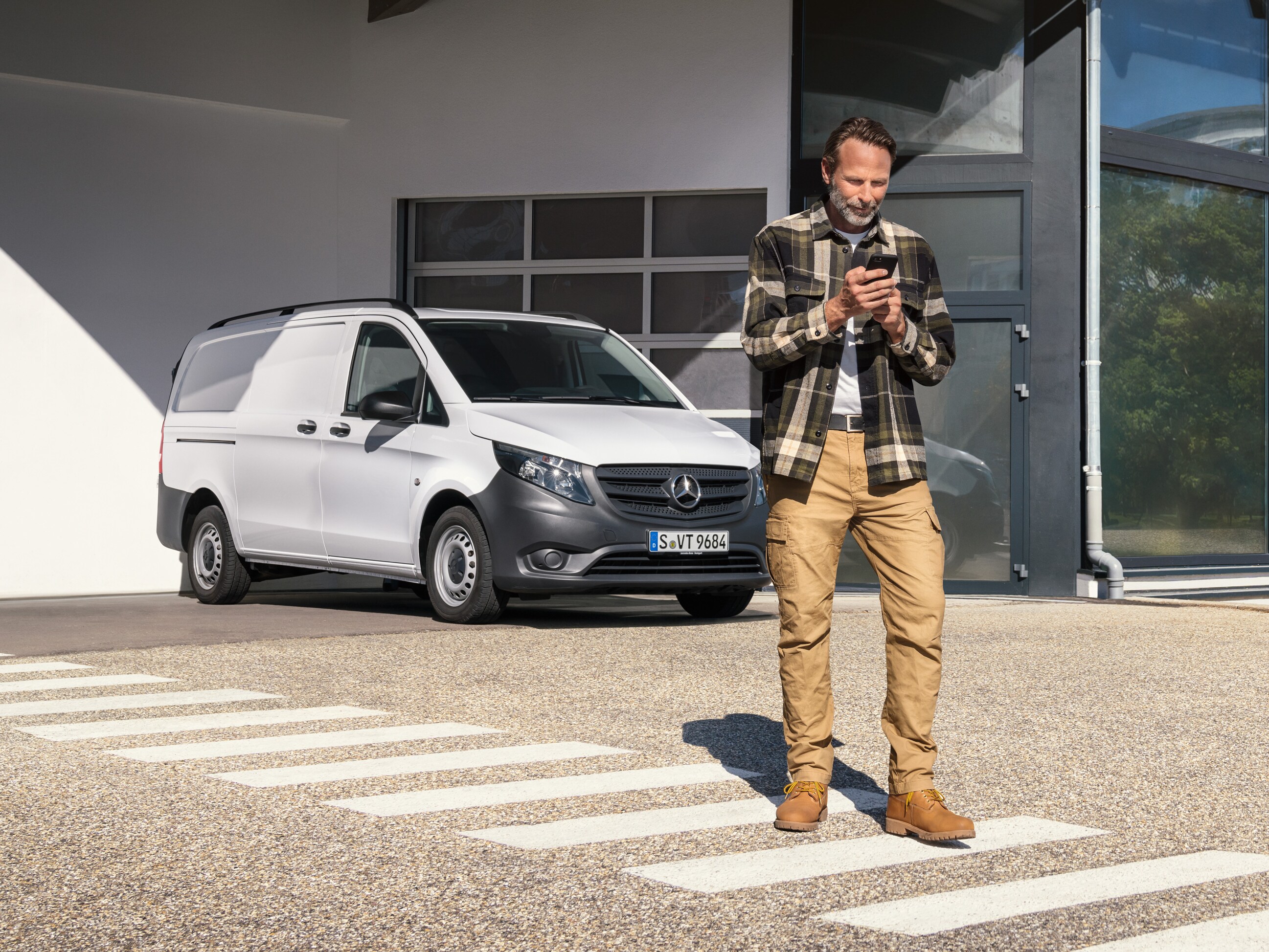 Mand står foran en hvid Mercedes-Benz Vito Varebil og bruger sin telefon.