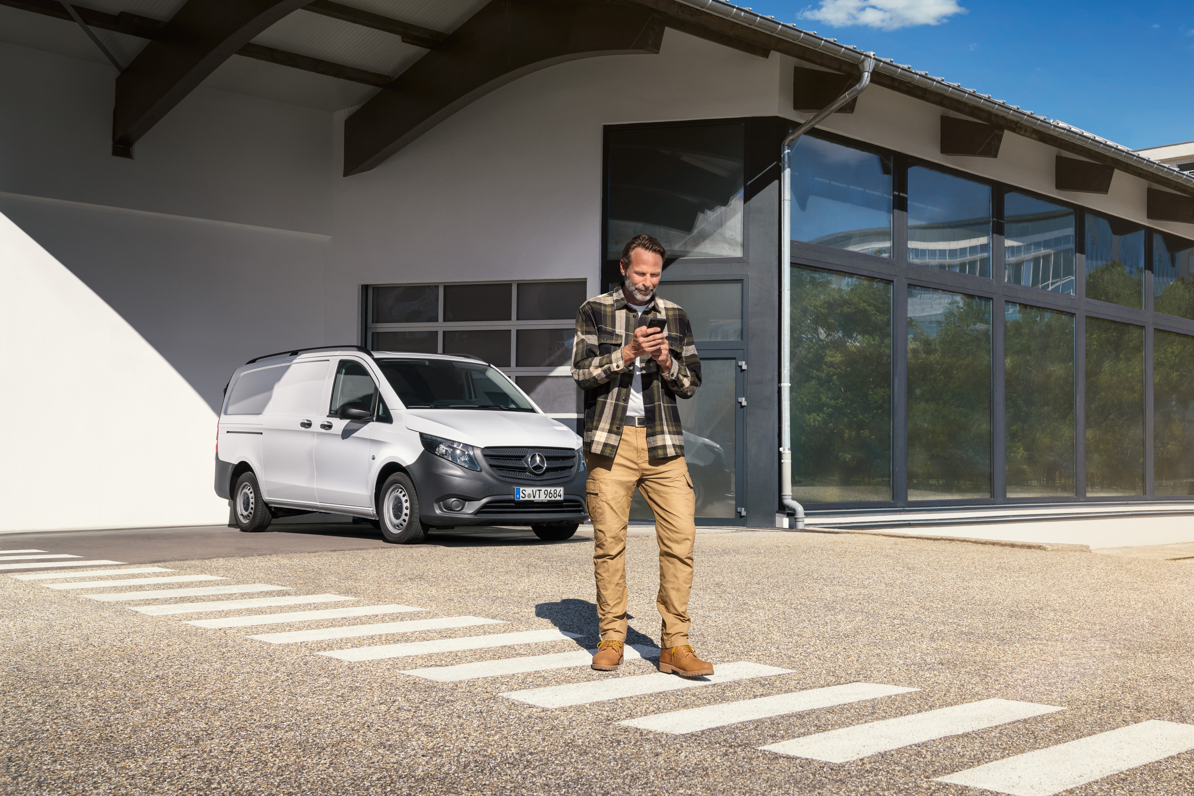 Mercedes-Benz | Service til elbiler | Digital support Mand står foran en hvid Mercedes-Benz Vito Varebil og bruger sin telefon.