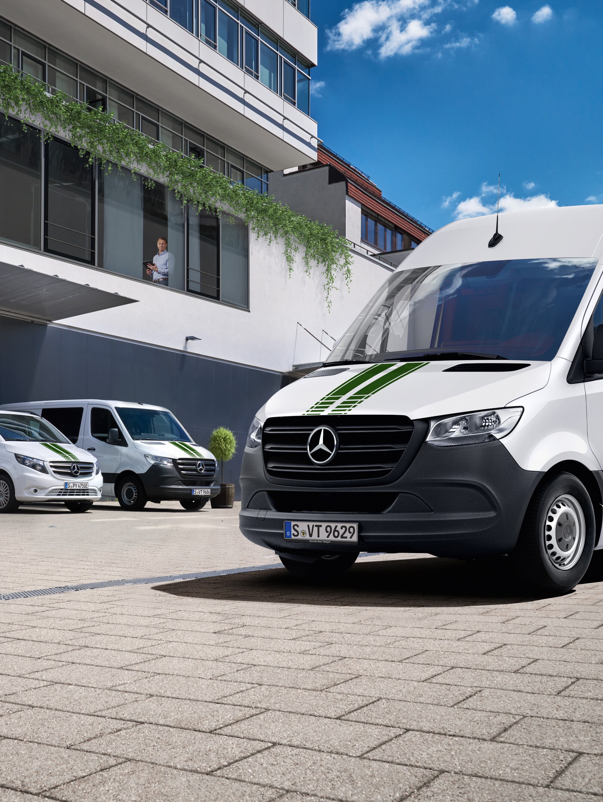 En flåde af hvide Mercedes-Benz varebiler foran en kontorbygning.