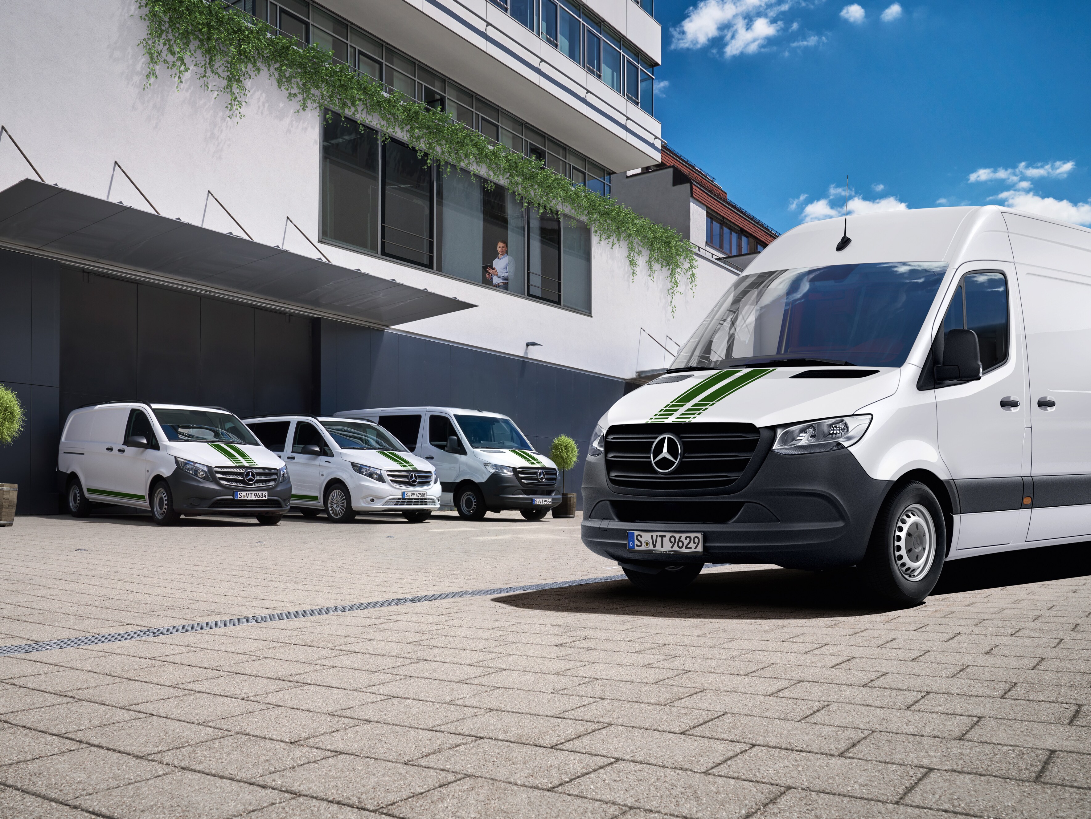 En flåde af hvide Mercedes-Benz varebiler foran en kontorbygning.