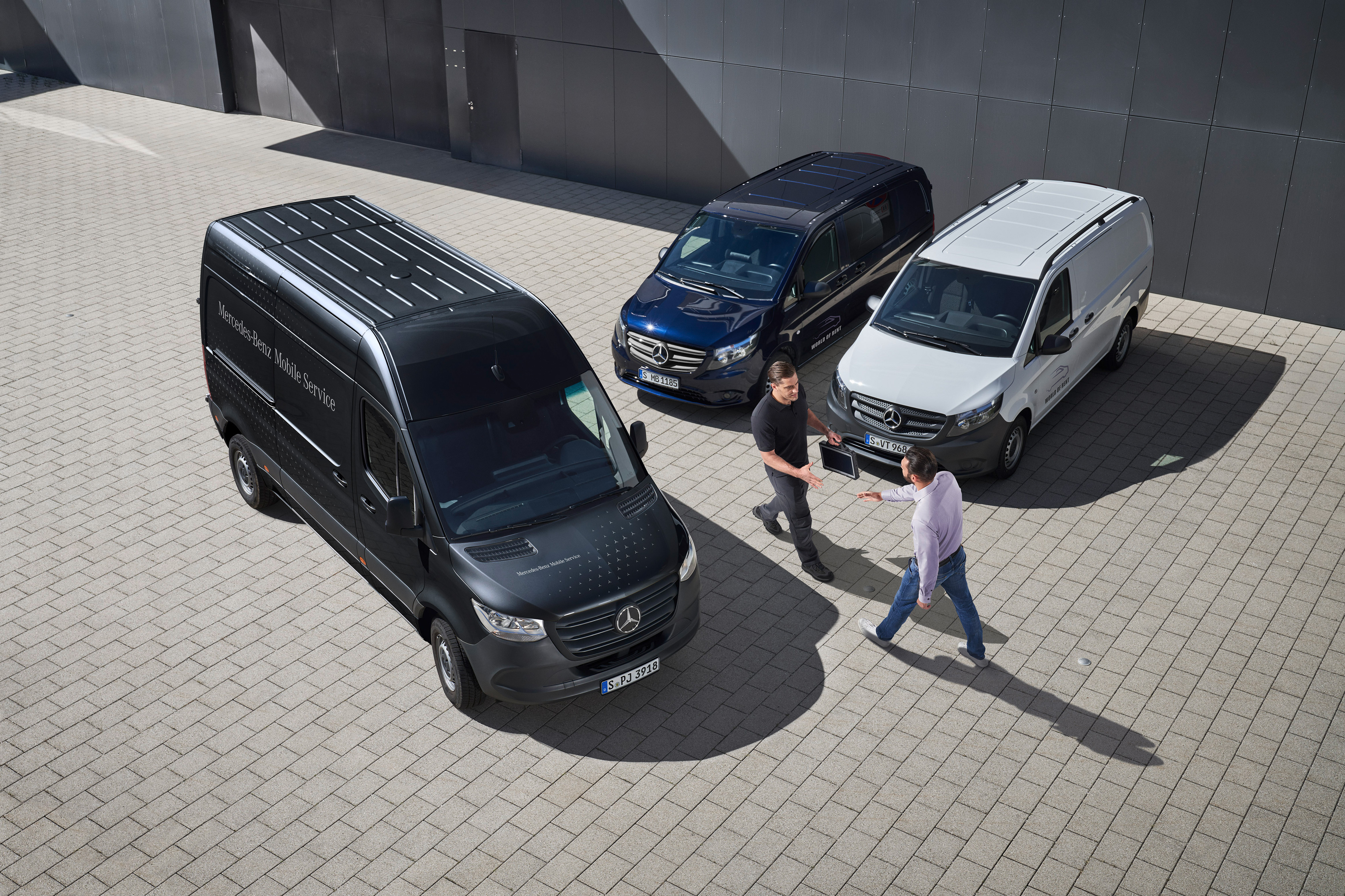 Mercedes-Benz | Varebilservice | Mobile Service To mænd hilser på hinanden blandt Mercedes-Benz varebiler på en parkeringsplads.