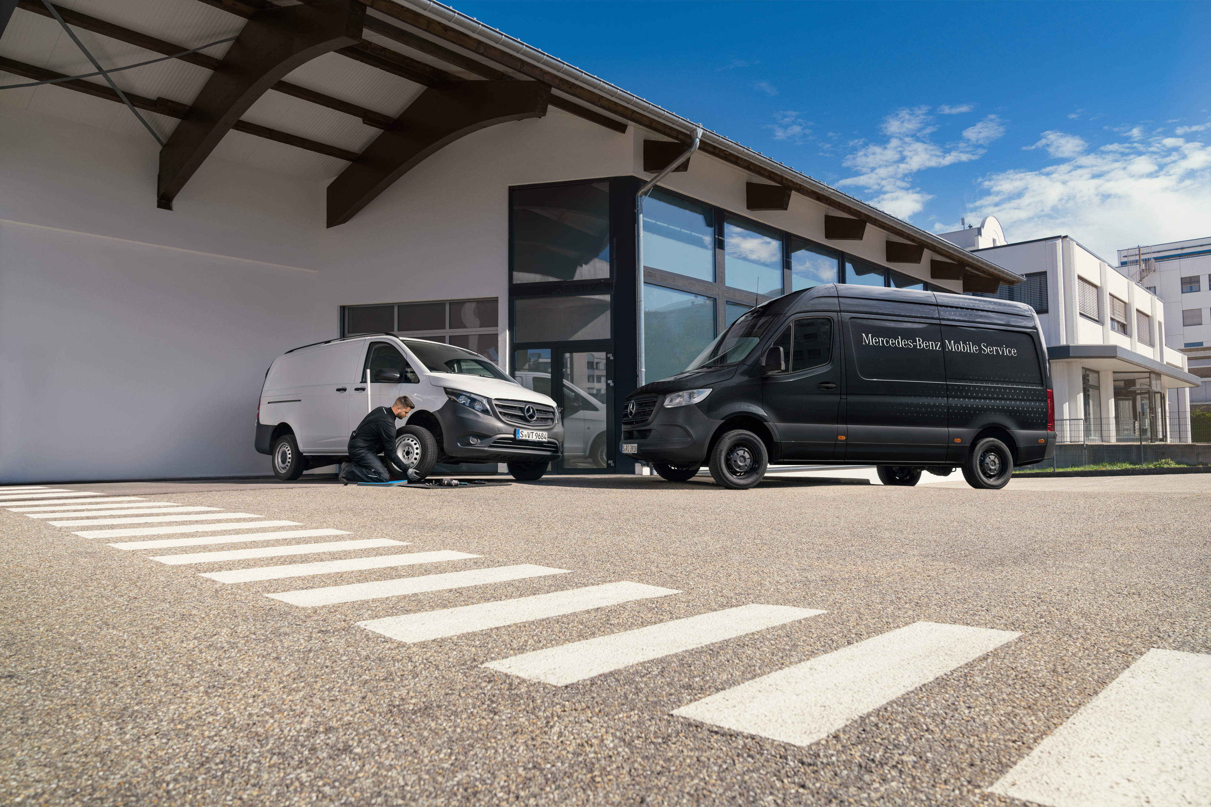 Mercedes-Benz | Mobile Service til varebiler | Bremsesystem Tekniker skifter et dæk på en hvid Mercedes-Benz Vito varebil foran et showroom.