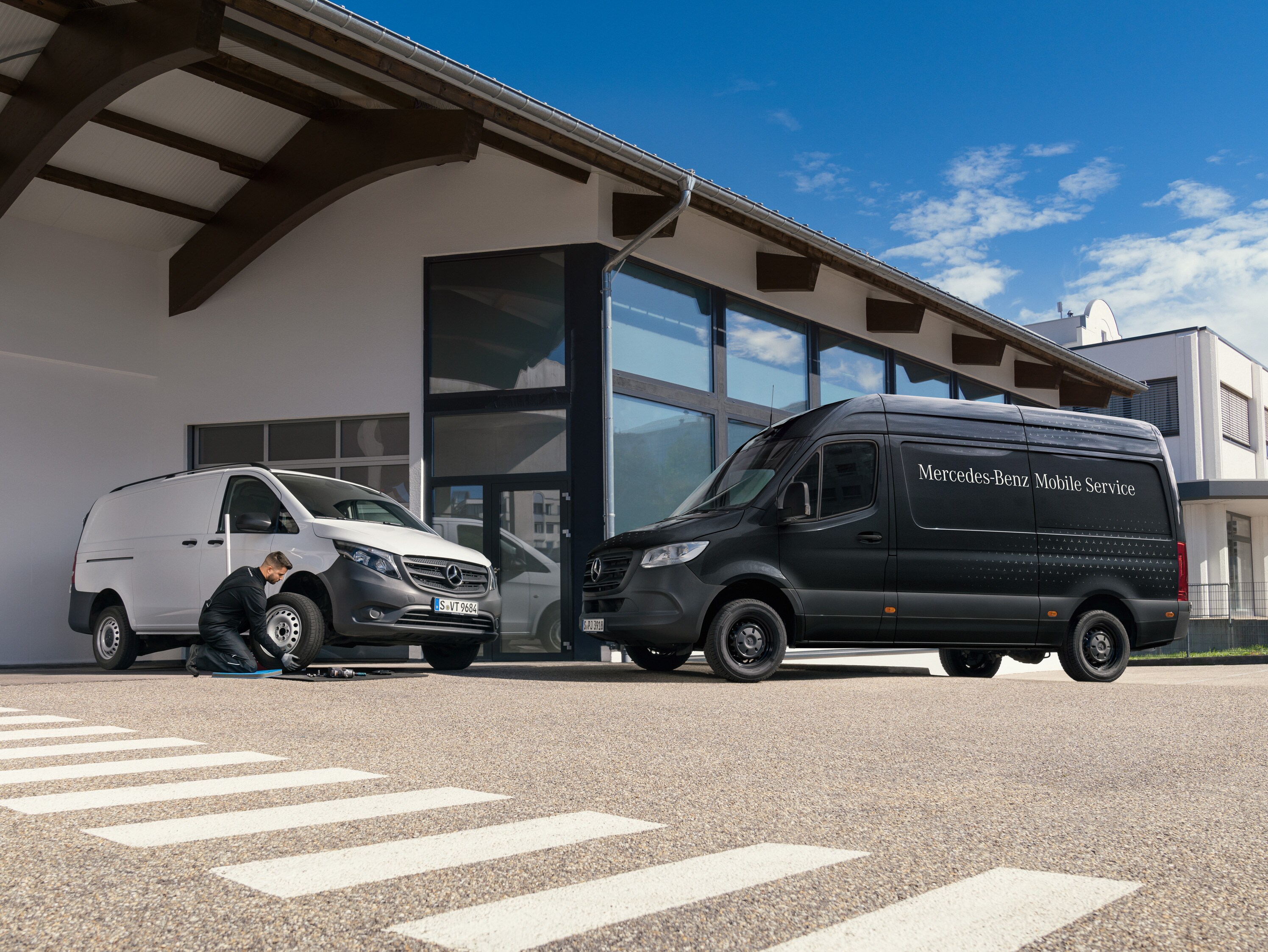 Tekniker skifter et dæk på en hvid Mercedes-Benz Vito varebil foran et showroom.