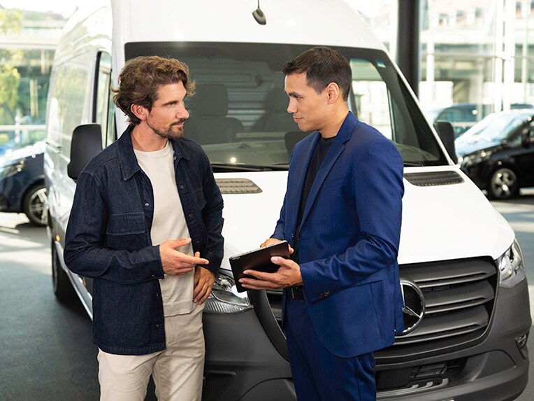 To mænd taler og peger på en tablet, mens de står foran en Mercedes-Benz varebil. 