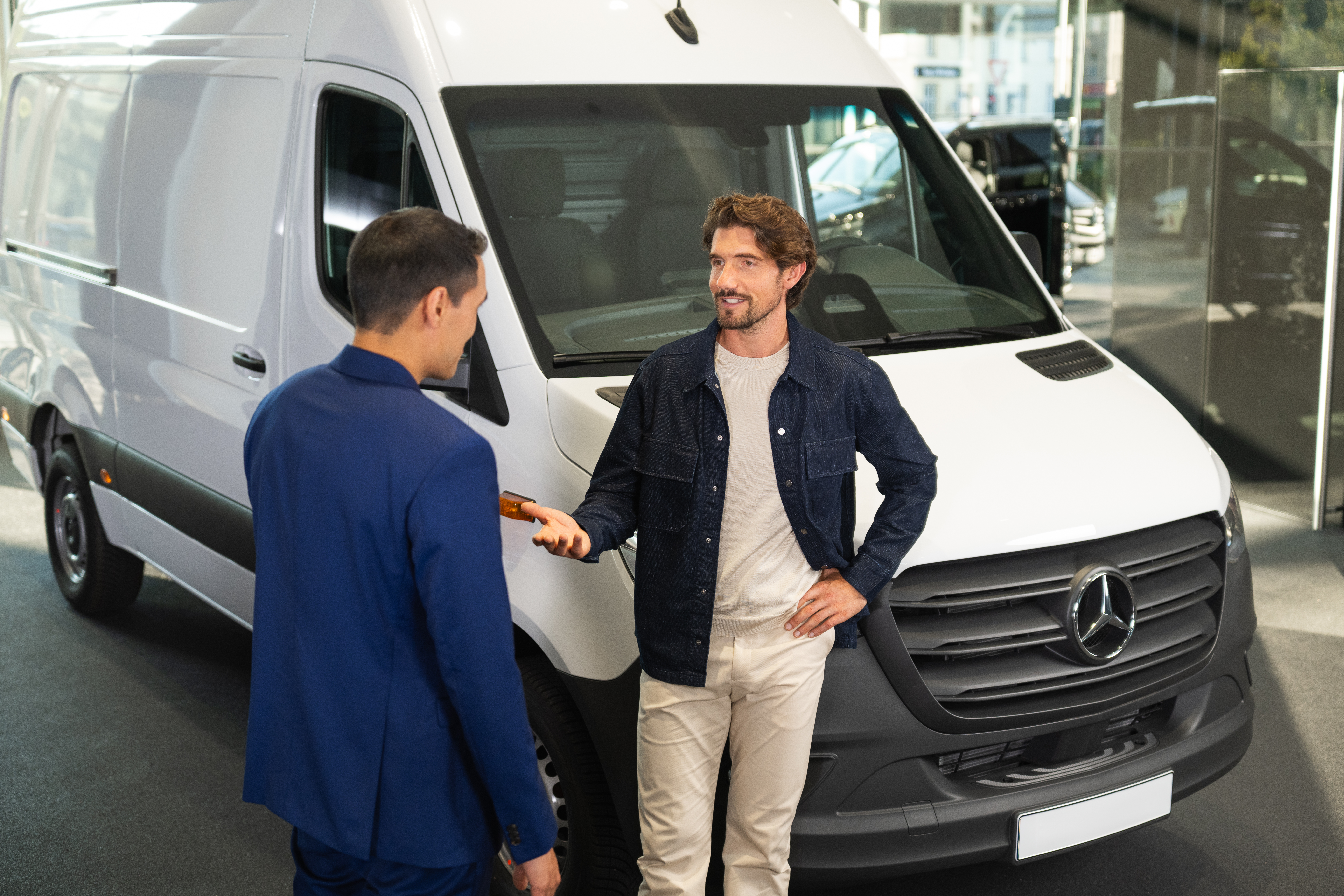 Ny Sprinter og eSprinter hæver standarden | Mercedes-Benz Vans Mercedes-Benz kunderådgiver i samtale med kunde foran hvid Sprinter Kassevogn