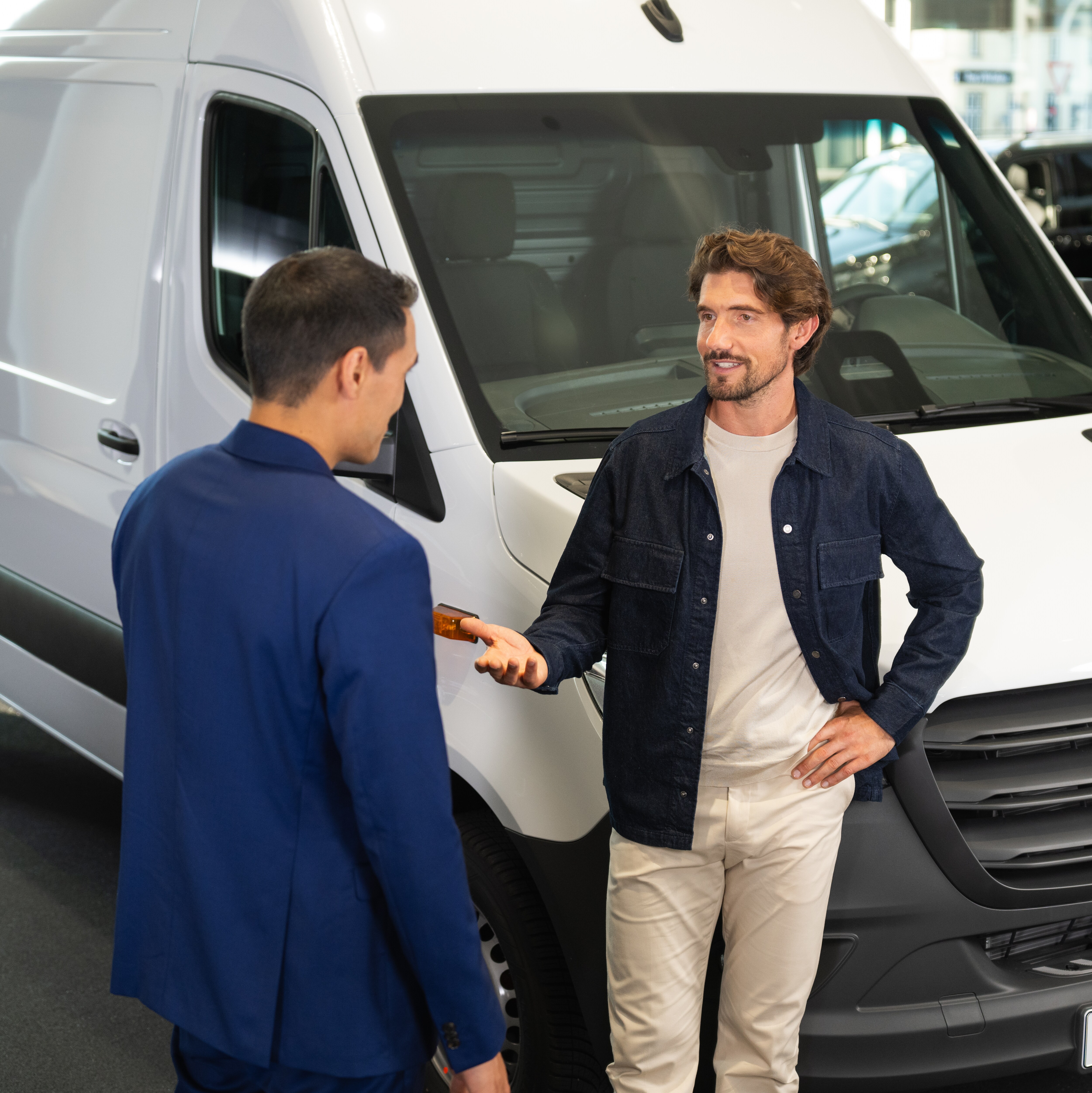 En mand læner sig mod en Mercedes-Benz varebil og har en samtale med en anden mand.